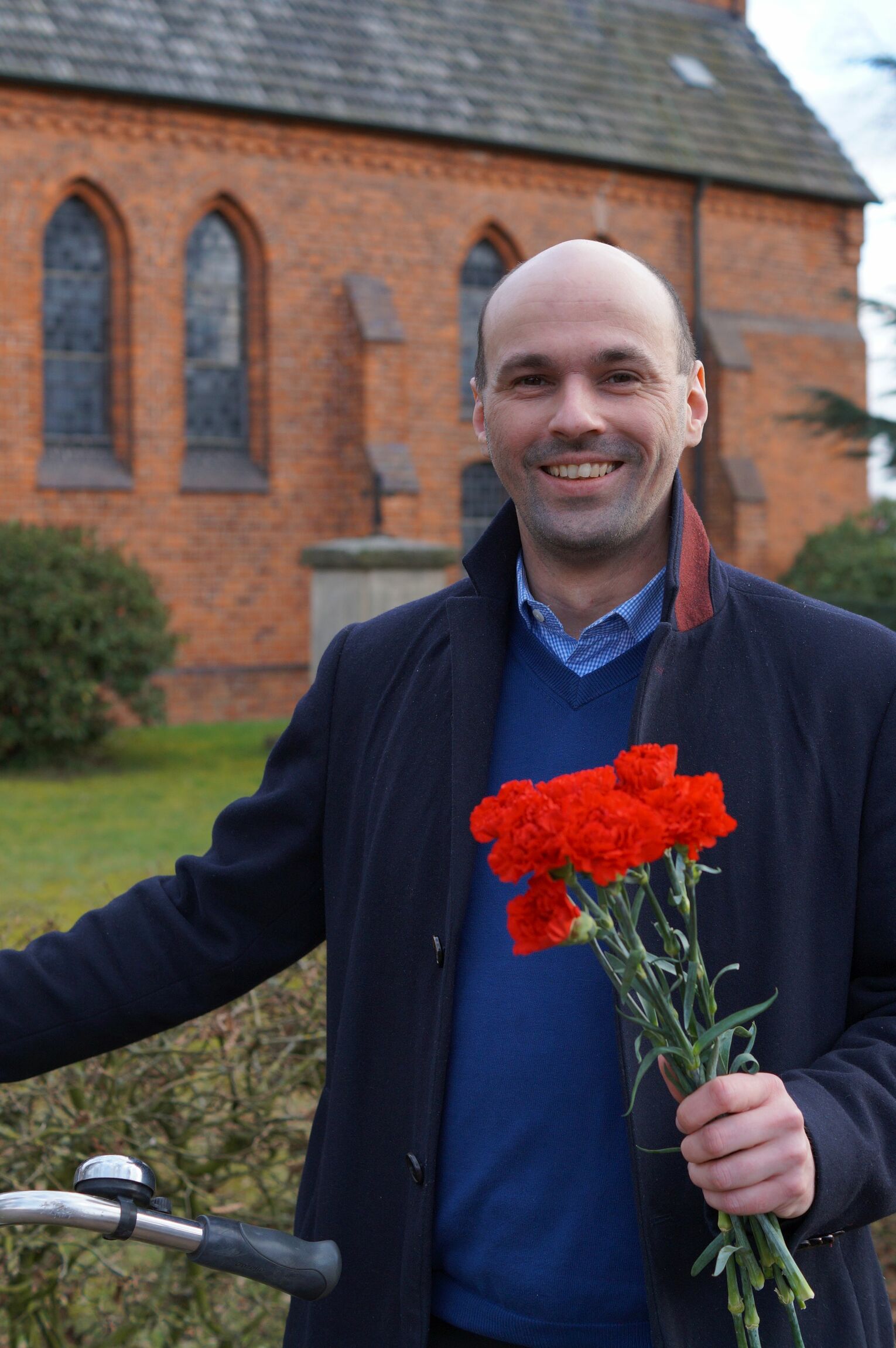 Grüße zum Frauentag. Pastor Florian von Issendorf radelt mit roten Nelken durch seine Gemeinde. Foto: Privat.