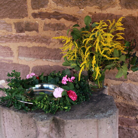 Eine Taufschale mit Blumenschmück an der Klostermauer