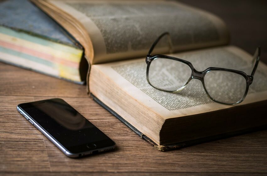 Brille auf Buch neben Telefon