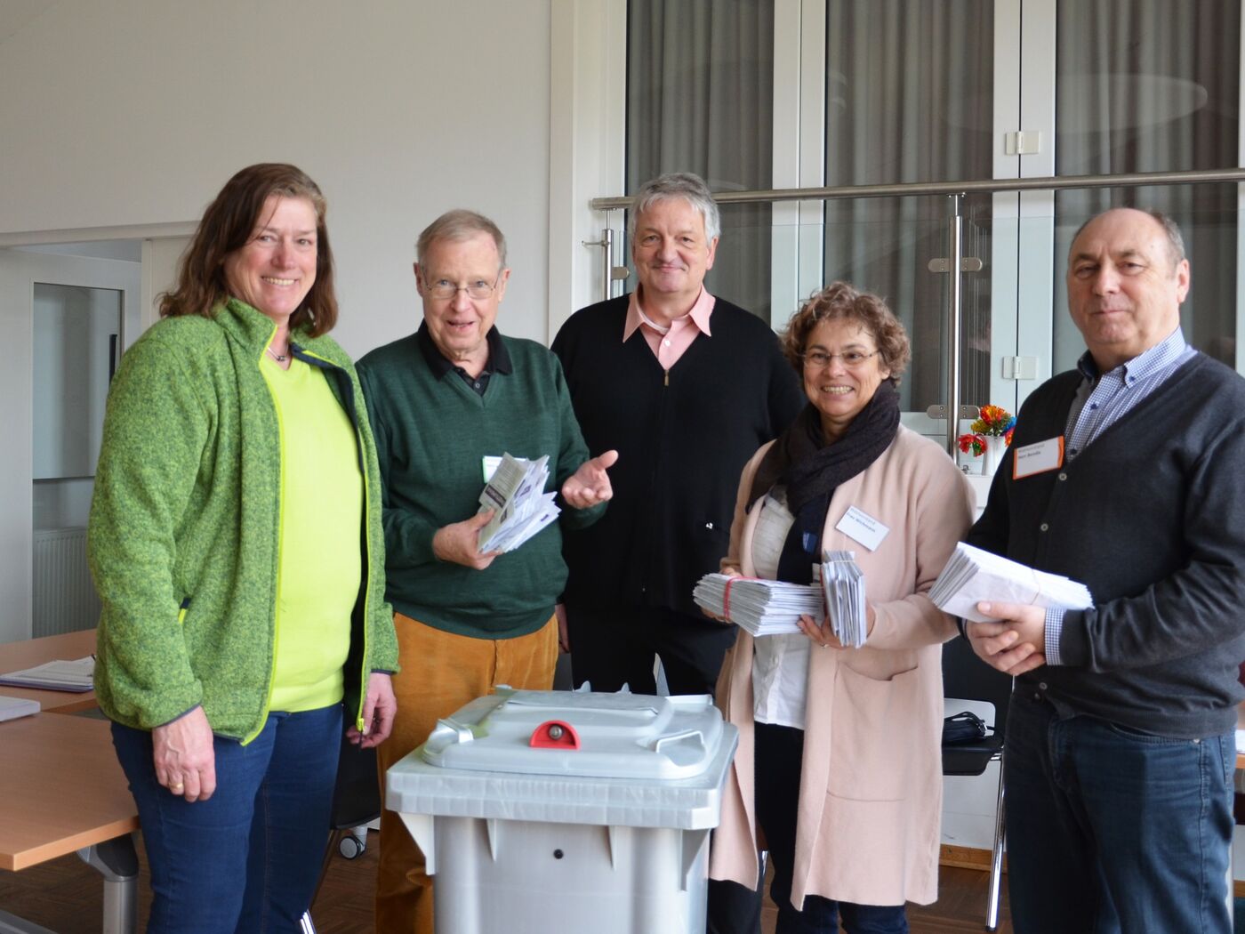 eine Gruppe von Menschen in einem Wahllokal. Sie halten Stimmzettel in der Hand.